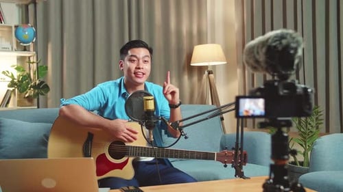 Asian Male With Guitar Talking To Camera While Live Streaming For His Social Media Channel