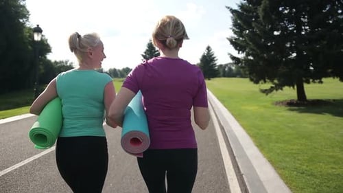 Two Women Walk with Yoga Mats in Park