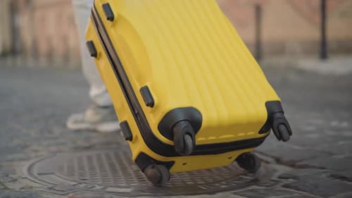Camera Follows Yellow Travel Bag Rolling on Pavement on City Street. Unrecognizable Male Tourist