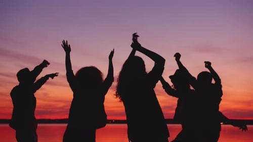 Estudiantes alegres bailando juntos en la playa al atardecer en una fiesta al aire libre