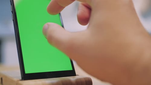 Man Touches and Looks at the Screen of the Black Smartphone with a Green Screen. Close Up