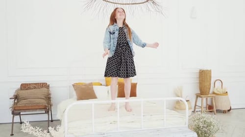 Red-Haired Girl Joyfully Jumping on Bed Indoors