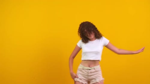 Stylish Young Woman Dancing Vigorously on Yellow Background