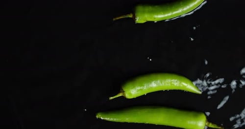 Green Chili Peppers Falling in Water Splashes.