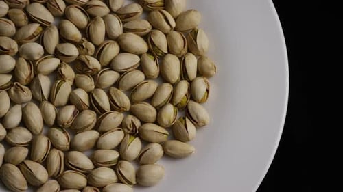Pistachios Rotating on White Plate, Black Background