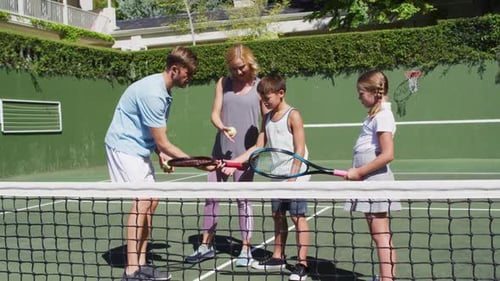 Caucasian father and mother teaching their kids to play tennis at tennis court on a bright sunny day