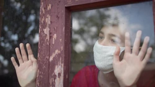 Teen Wearing Mask Looking Out Window at Home