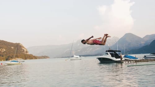Junger Mann springt vom Sprungbrett in Mountain Lake Zeitlupe ins Wasser