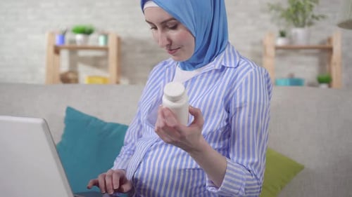 Pregnant Woman with Pills Using Laptop on Couch