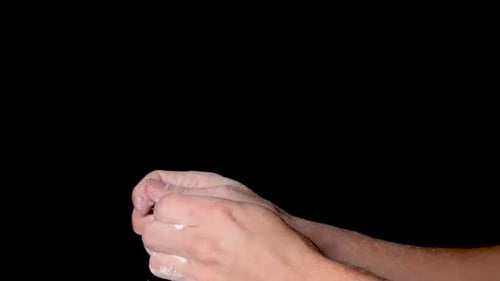 Eine Person reibt sich die Hände und verteilt das Kreidepulver gleichmäßig, isoliert auf schwarzem Hintergrund.
S
