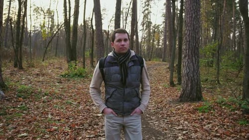 Erwachsener Mann mit schwarzen Haaren und Rucksack, der im Herbstwald spazieren geht.