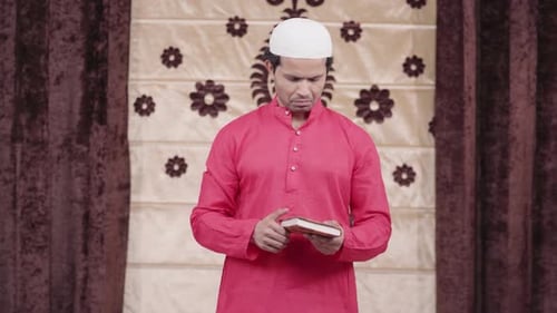 Man Reading from Book in Front of Drapes