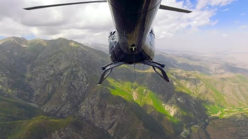 Helicopter View From the Tail Section Flying Over Rocky Mountains with Clouds on Peaks