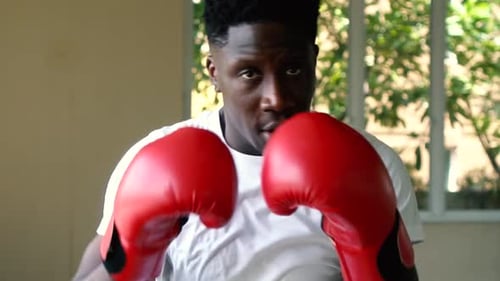Athletic Sporty African American Male Boxer in Red Boxing Gloves Punching During Workout at Gym