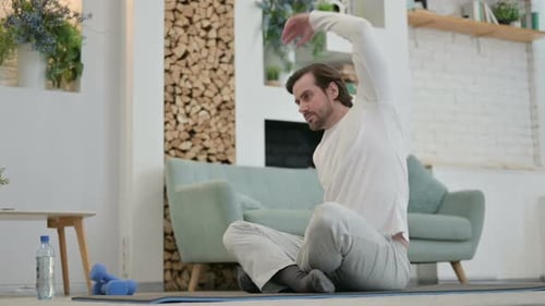 Man Stretching Body Seated on Yoga Mat Indoors