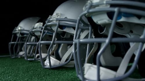 Football Helmets Lined Up on Field in Dark