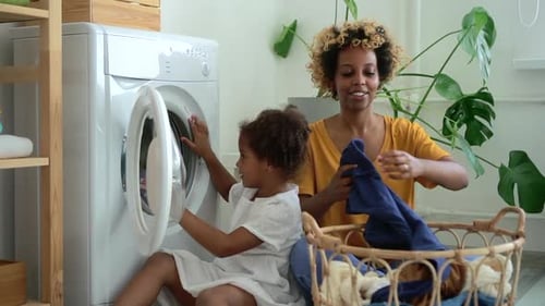 Young Mom and Laundry Wash Machine Cloth Little Daughter Loading Washing Machine While Sitting on