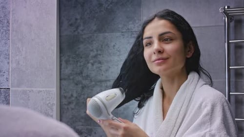 Woman Styling Wet Hair with Hair Dryer in Bathroom