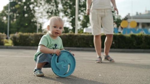 Smiling Toddler Playing in Amusement Park. Cute Kid Throwing Frisbee Outside