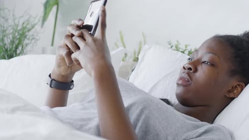 Young Woman Using Phone While Lying in Bed