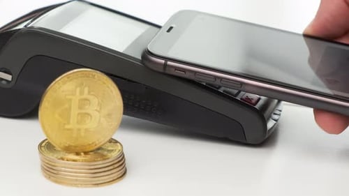Nahaufnahme: Kontaktloses Bezahlen per Smartphone und Bitcoin-Münzen auf dem Tisch
