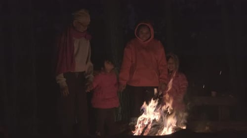 Family warms near campfire in forest and having.