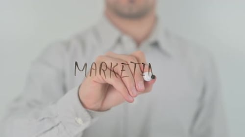 Man Writes the Word Marketing on Clear Surface