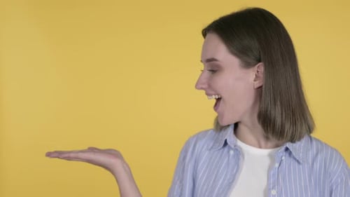 Smiling Woman Presenting Product Against Yellow Background