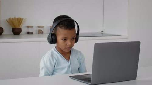 Boy Watches Laptop with Headphones in Kitchen