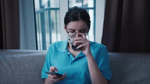 Young Woman Using Phone, Drinking Coffee at Home