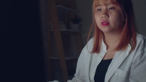 Young asian woman working late using desktop on desk in living room at home.
