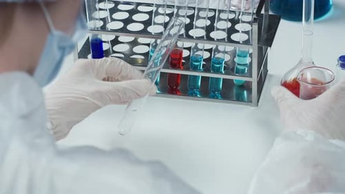 Doctor Wearing Protective Mask Gown Gloves Pouring Red Solution Into Flask and Putting Into Stand