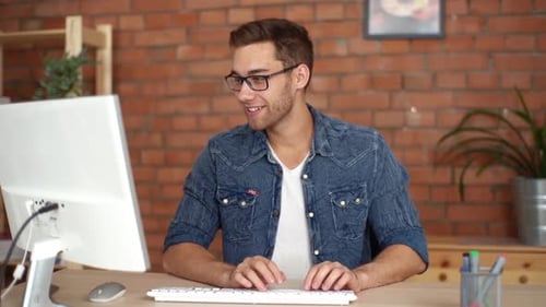 Smiling Young Adult Typing at Computer