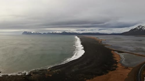 Drone Over Black Sand Beach With Mountain Range In Background