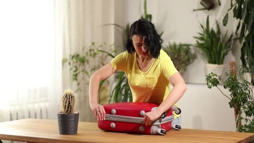 Woman close and zips red suitcase, packing, getting ready for summer vacation