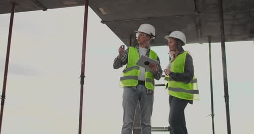 Two Engineers a Man and a Woman with a Tablet Computer at a Construction Site Condemn the