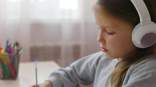 Girl Wearing Headphones Writes at Desk