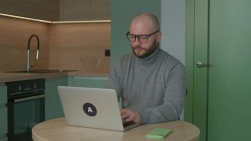 Man Working on Laptop at Table in Apartment