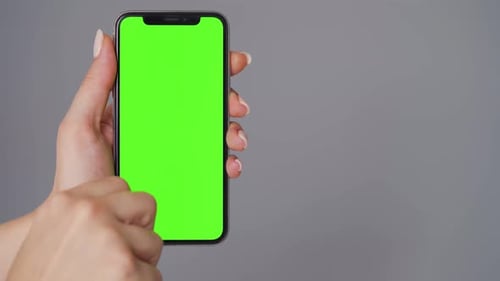 Female Hands Using a Smartphone with a Green Screen on a Gray Background. Chroma Key