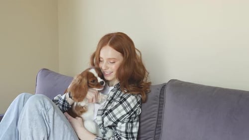 Woman Cuddles Dog Indoors on Gray Couch