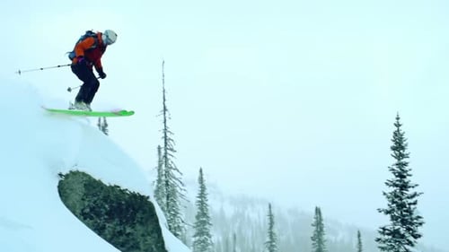 Skier Jumps off Snowy Rock in Mountain Forest