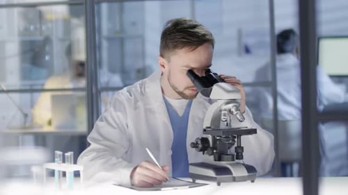 Scientist Using Microscope and Taking Notes in Lab