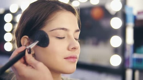 Closeup View of Female Hands Applying Facial Powder on Young Woman's Skin Using Special Brush