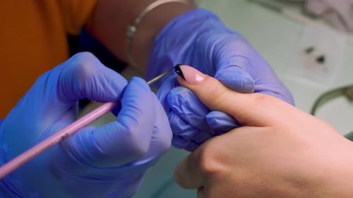 close-up of a manicurist paints a black French on the client's nails with a brush.