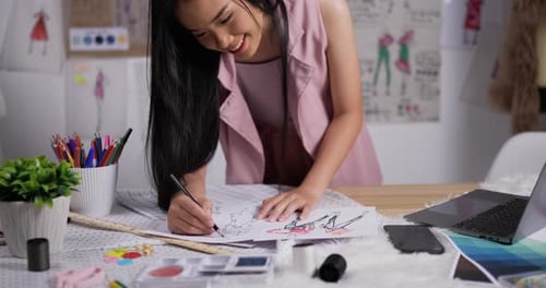 Fashion Designer Sketching Dress Designs at Desk