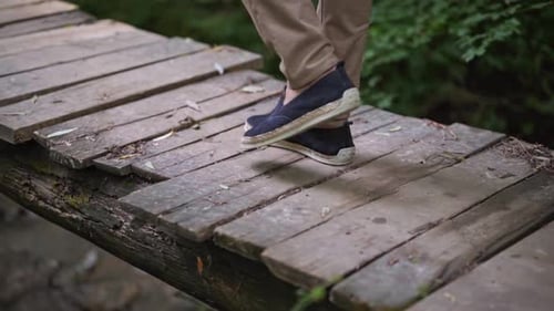 Man take walk on wooden bridge. Man legs on old wooden bridge through small river