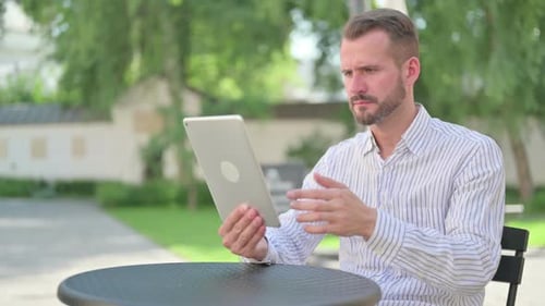 Middle Aged Man Reacting to Loss on Tablet in Outdoor Cafe