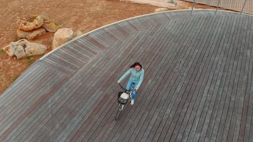 Woman Is Riding Bicycle Outdoors on Wooden Path in Park in Summer, Aerial View