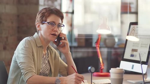 Businesswoman Talking on Phone and Taking Notes in Office