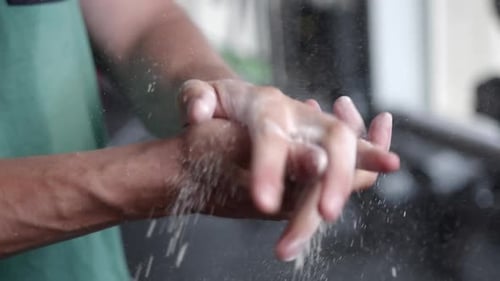 A man in a gym rubbing chalk over his hands with cotton while preparing for a workout